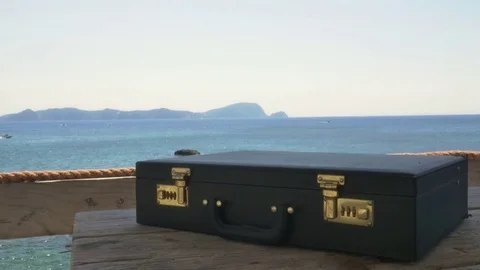 Briefcase on a wooden table with sea in the background Vídeo Stock 77626645