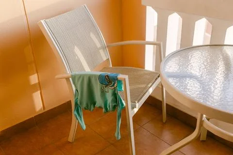 Bright and inviting balcony featuring a sunlit chair with a colorful garment Stock Photos