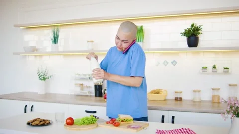 In a bright and modern kitchen, a bald woman who survived cancer wearing a blue Stock Footage 293869253