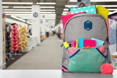 Bright backpack with school stationery on table in shopping mall. Space for t 库存照片