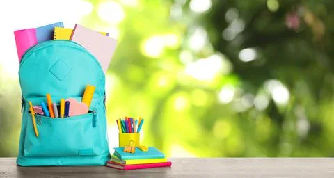 Bright backpack with school stationery on table against blurred green backgro Stock Photos