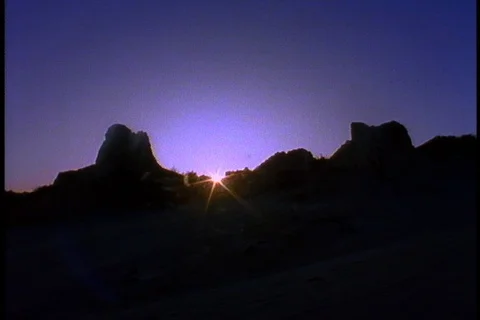 Bright ball of sun rises behind silhouette of jagged mountains or hills. Stock Footage 86752760