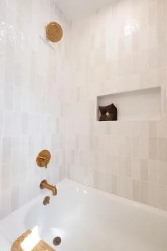 Bright bathroom interior showcasing light tiling, recessed shelf, and bronz.. 스톡 사진