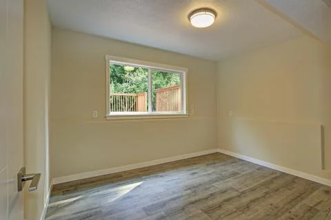 Bright beige large empty room with hardwood floor and a small window. America Stock Photos