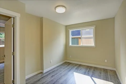 Bright beige large empty room with hardwood floor and a small window. America Stock Photos