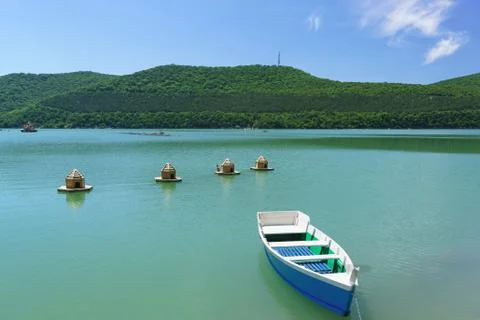 Bright blue empty rowing boat and duck houses on the emerald water of the mou Stock Photos