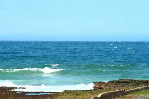 Bright Blue Ocean Waves Crashing Against The Rocky Shoreline On A Clear Day Stock Photos