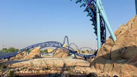 Bright blue roller coaster rushes through loops and curves in a desert-themed Stock Footage 311195161