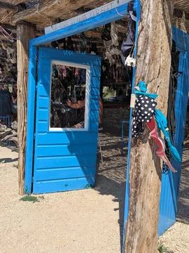 Bright blue rustic beach bar entrance with hanging swimwear and weathered woo Stock Photos