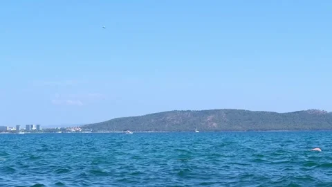 Bright blue sea with small waves in the foreground, with a hilly island and Stock Footage 285741135