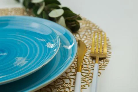 Bright blue serving plates stand on a golden napkin, a fork of gold and white Stock Photos