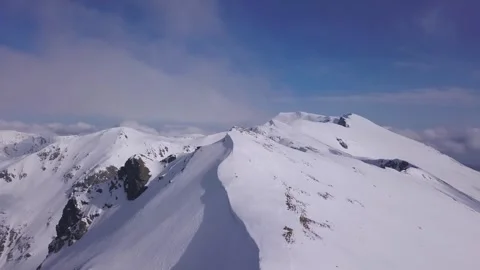 Bright blue sky and soft clouds over snow covered mountain peaks. Wide Video stock 252165252