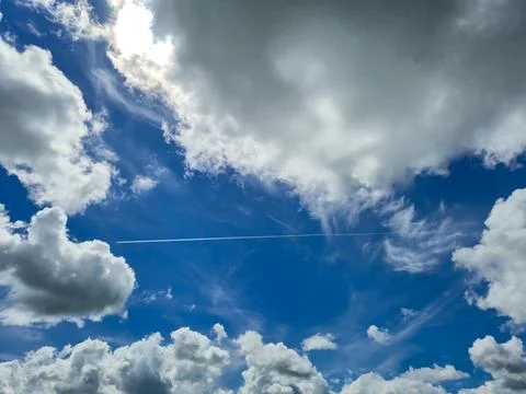 Bright blue sky with dramatic clouds and contrail Stock Photos