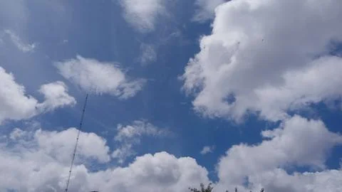 Bright blue sky with fluffy white clouds, tall radio antenna tower, flying birds 库存照片