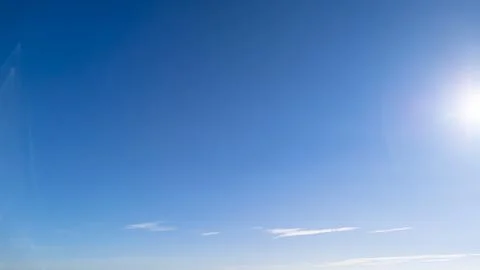 Bright blue sky with soft clouds and a radiant sun shining high above, creating Stock Photos
