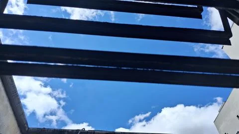 Bright blue sky viewed through dark horizontal metal window bars Stock Photos