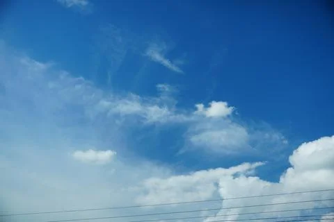 A bright blue sky with white clouds and power lines 스톡 사진
