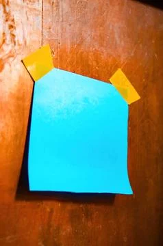 Bright blue sticky note taped to a rustic wooden wall with yellow tape, per.. Stock Photos