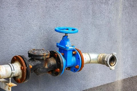 A bright blue valve is securely attached to a pipe on a wall Stock Photos