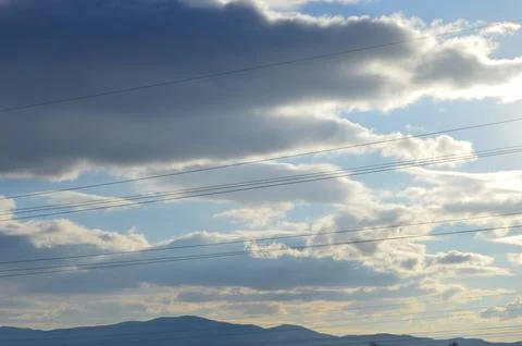 Bright clouds drift over mountainous landscape on a clear day, showcasing Stock Photos