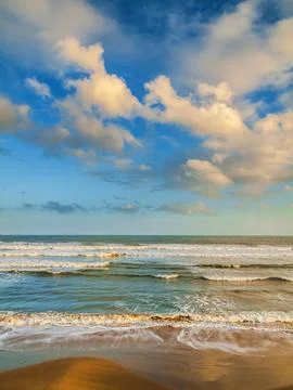Bright clouds over waves breaking onto a peaceful, sandy beach Stock Photos