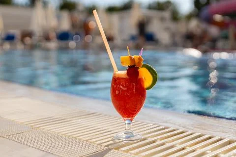 A bright cocktail sits on the edge of a pool. It has fruit garnishes and a .. Stock Photos