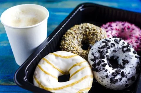 Bright colored doughnuts on a dark lining and a paper Cup of coffee Stock Photos
