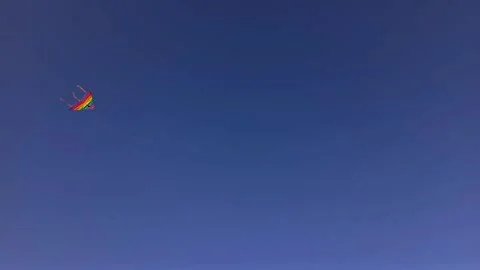 Bright colored triangular kite flying high in clear blue sky Video stock 268634820