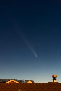 Bright comet with a long tail in the night sky above rooftops Foto stock