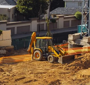 Bright compact backhoe loader on the surface preparation of construction site Stock Photos