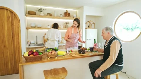 Bright, cozy kitchen where two women prepare a meal as an older man chats a.. Video stock 347672674