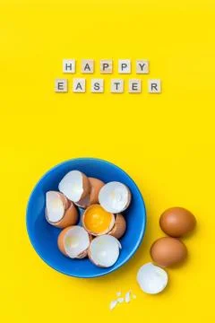 Bright creative postcard with happy Easter text. Raw eggs, yolk and shell in a Stock Photos