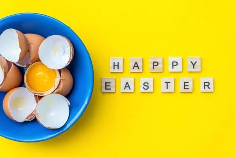 Bright creative postcard with happy Easter text. Raw eggs, yolk and shell in a Stock Photos