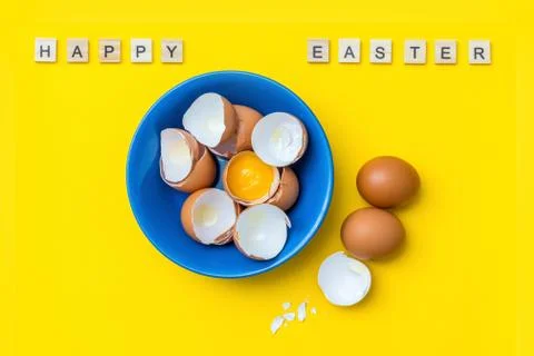 Bright creative postcard with happy Easter text. Raw eggs, yolk and shell in a Stock Photos