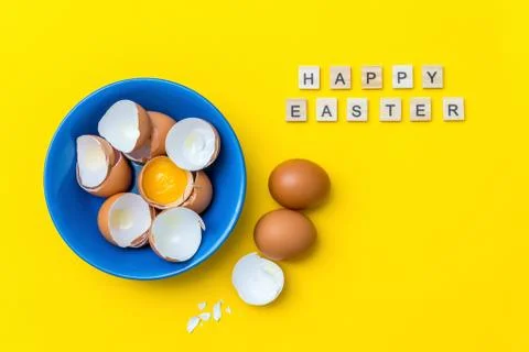 Bright creative postcard with happy Easter text. Raw eggs, yolk and shell in a Stock Photos