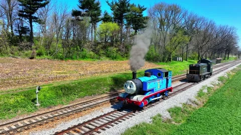 A bright day shows a blue train moving on tracks. Smoke rises from the train as Stock Footage 336116548