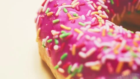 Bright donut in a pink glaze with a multi-colored rainbow sprinkle on a pink Stock Footage 150964194