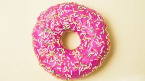 Bright donut in a pink glaze with a multi-colored rainbow sprinkle on a pink Stock Footage 150964236