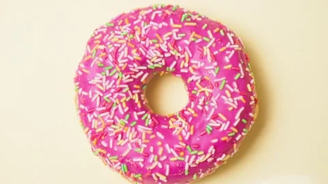 Bright donut in a pink glaze with a multi-colored rainbow sprinkle on a pink Stock Footage 151033711