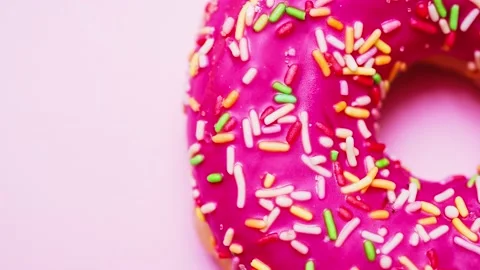 Bright donut in a pink glaze with a multi-colored rainbow sprinkle on a pink Stock Footage 151219211