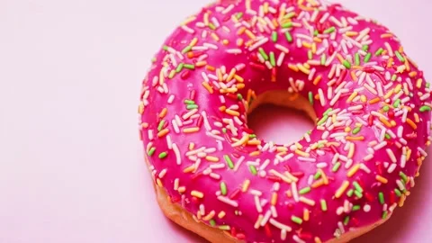 Bright donut in a pink glaze with a multi-colored rainbow sprinkle on a pink Stock Footage 151281575