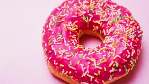Bright donut in a pink glaze with a multi-colored rainbow sprinkle on a pink Stock Footage 151346739