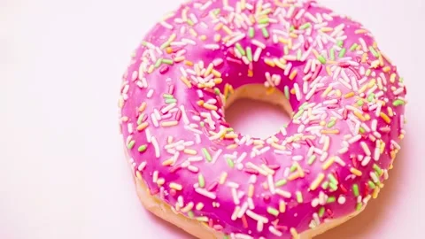 Bright donut in a pink glaze with a multi-colored rainbow sprinkle on a pink Stock Footage 151413146
