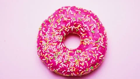 Bright donut in a pink glaze with a multi-colored rainbow sprinkle on a pink Stock Footage 151474898