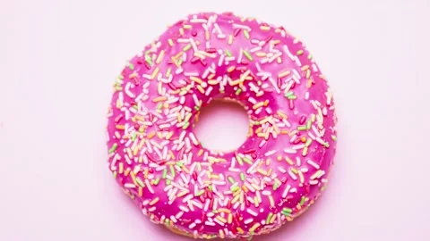 Bright donut in a pink glaze with a multi-colored rainbow sprinkle on a pink Stock Footage 151542890