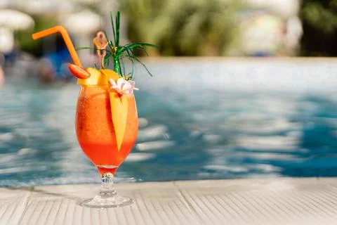 A bright drink is placed on a white surface near a pool. The drink is decorat Stock Photos