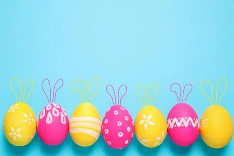 Bright Easter eggs with cute bunny ears and space for text on light blue back Stock Photos