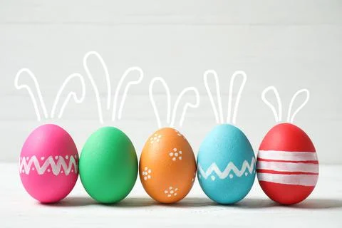 Bright Easter eggs with cute bunny ears on white table Fotos de archivo