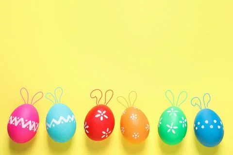 Bright Easter eggs with cute bunny ears and space for text on yellow backgrou Foto stock