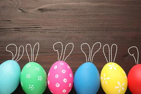 Bright Easter eggs with cute bunny ears and space for text on wooden backgrou Stock Photos